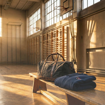 Un sac de sport et un sweat plié sur un banc, dans un gymnase éclairé par la lumière du soir